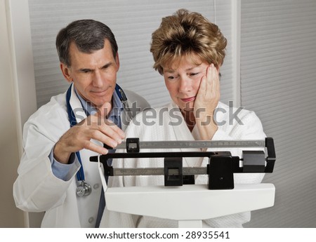 Woman looking dismayed at her weight as she is weighed by her doctor on a medical scale.