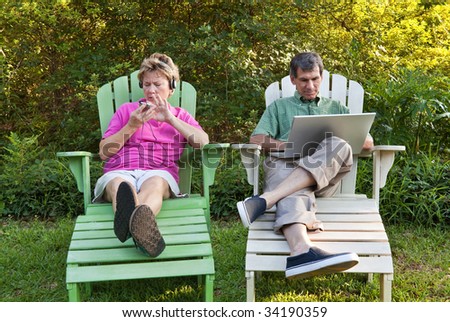 Couple outdoors relaxing...each busy with his own technology (laptop and MP3). Some motion blur.