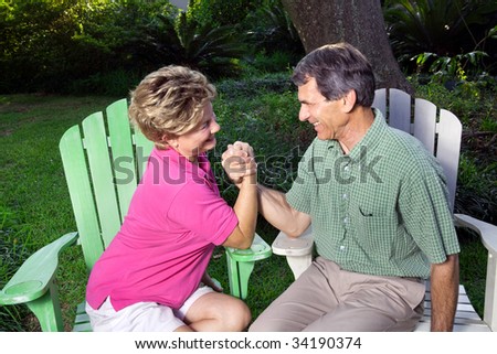 Laughing, happy couple arm wrestling in a green outdoor setting