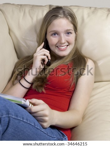 Portrait of a pretty young woman taking on her cellphone while reclining on a couch, reading or studying her notes.