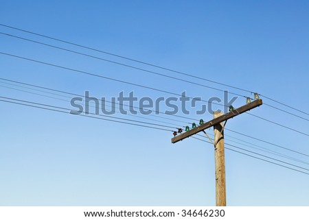 Distance shot of early 20th century, weathered telephone pole with glass insulators and unwrapped copper wires. Lots of sky, good background shot.