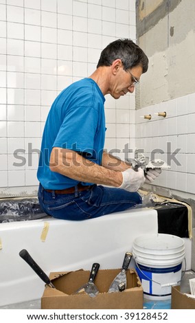 Man applying ceramic tile to a bathtub enclosure wall.