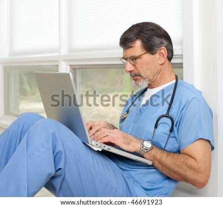 Mature doctor sitting on floor reviewing data on his laptop computer. Light and bright exposure.