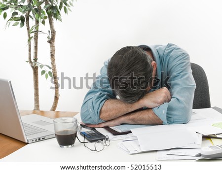 Man at office desk in with his head on his arms, worrying about paying the bills.