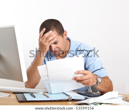 Young man at desk with computer and checkbook, worrying about paying bills, holding his head.