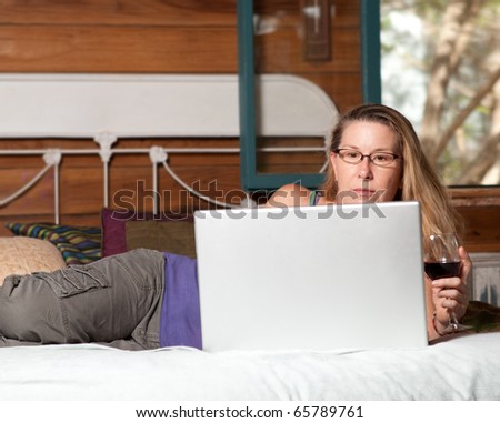 Pretty mature woman, surfing the internet while enjoying a glass of red wine in her mountain cabin.