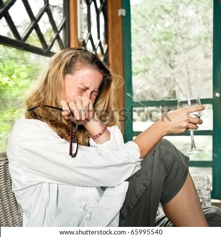 Pretty mature woman either laughing uproariously or crying in sorrow, holding glass of red wine.