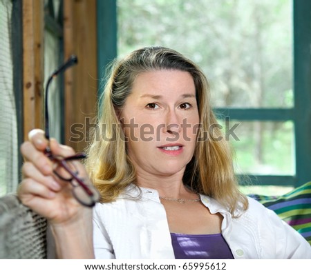 Mature woman holding her eyeglasses and looking directly at the viewer with a look of worry, concern, surprise or disbelief.