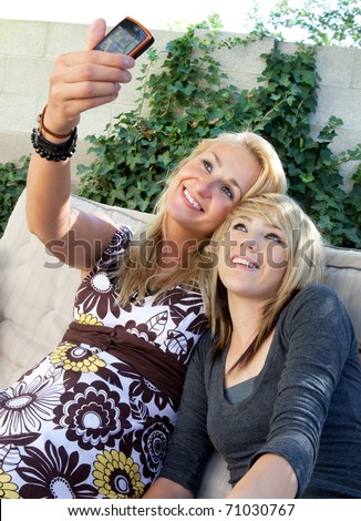 Cute blonde mother and teenage daughter taking their picture with a mobile cell phone camera.