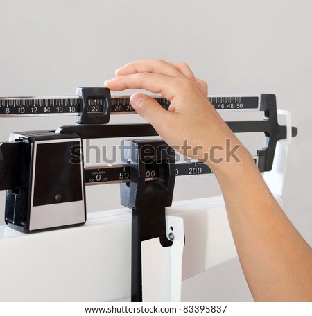 Closeup view of woman\'s hand adjusting professional balance weight scale. View is closeup, with a neutral background.