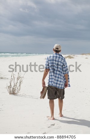 Man walking on a white sandy beach with a storm approaching.