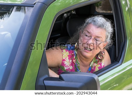 Angry senior woman driver with road rage yelling out car window.