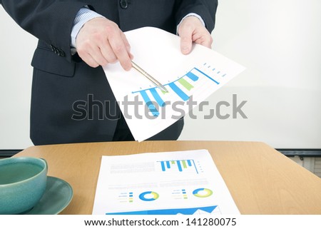 Man in Suit Pointing Charts with Pen