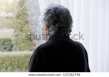 Elderly woman looks out of her window
