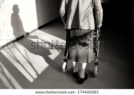 Elderly woman with walker in a hallway, black and white