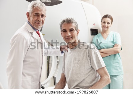 Happy senior doctor with his male patient at CT scanner machine. Female assistant on background.