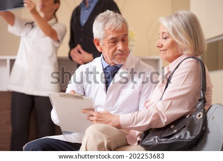 Doctors and patients in hospital waiting room. Senior male doctor explaining medical exams to woman patient.