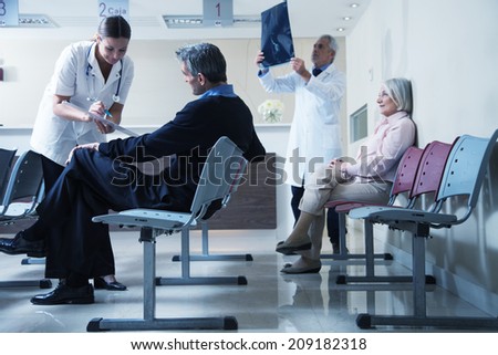 Doctors reviewing x-ray at hospital reception while people sitting in background.