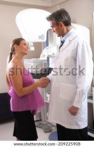 Happy young female patient handshaking doctor while undergoing mammogram x-ray test.