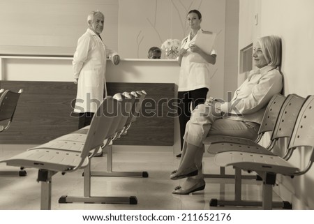 Senior woman patient seated in the hospital waiting room with medical personnel at the desk.
