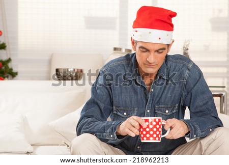 Man with Santa hat in deep thoughts at home with a cup of tea.