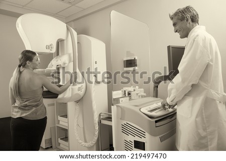 Female patient undergoing scan at mammography machine with male doctor supervisor. Happy hospital scene.