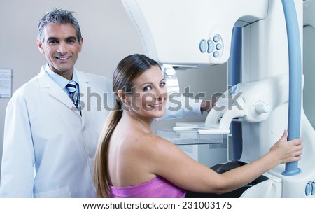 Young woman in 30s undergoing scan at mammography machine with happy male doctor. Health concept.
