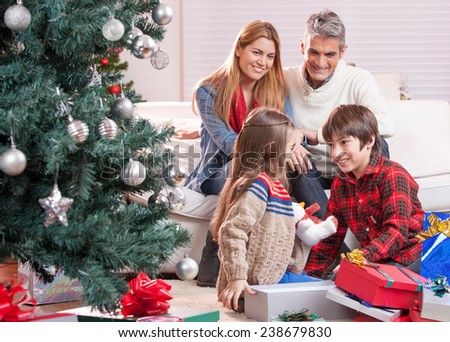 Brother and sister exchanging Christmas gifts in front of their parents. Happy family and holiday concept.