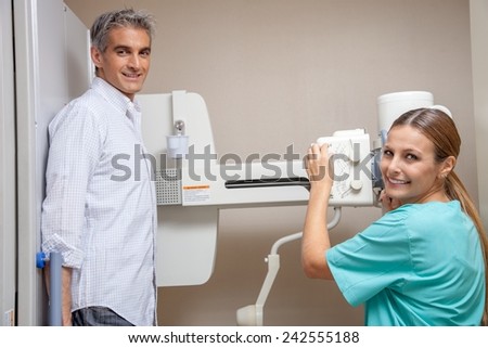 Male patient in 40s undergoing x-ray test assisted by smiling beautiful female doctor. Happy hospital scene concept.