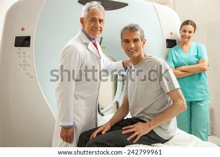 Man in 40s ready to undergo MRI scan, assisted by two smiling doctors.