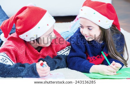 Happy brother and sister laying and writing with Christmas hat.