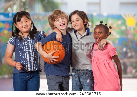 Happy multi ethnic elementary kids playing basketball in school courtyard