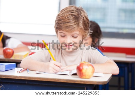 Happy student at elementary school writing on his exercise book.