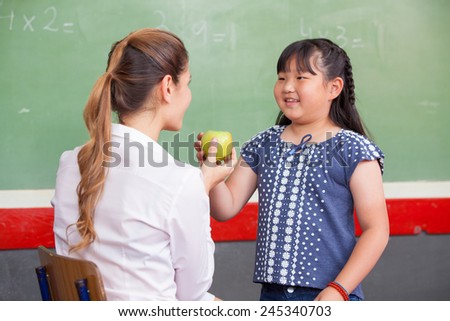 Happy teacher and asian elementary female student touching a green apple.