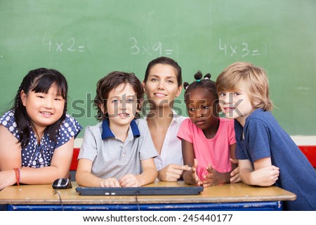 Happy female teacher with her multirace classroom at school desk.