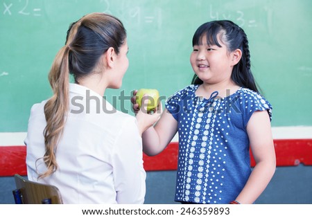 Happy teacher and asian elementary female student touching a green apple.