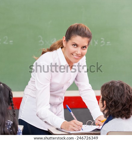 Happy female teacher checking students homework at school.