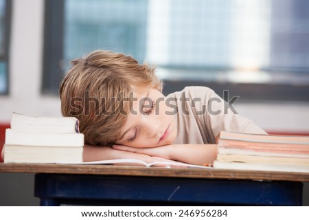 Tired child sleeping while studying in the primary school classroom.