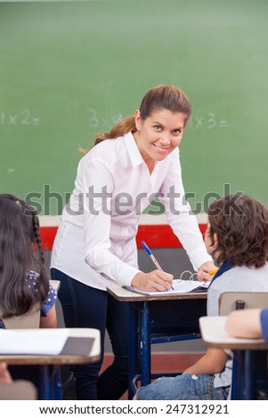 Happy female teacher checking students work at primary school.