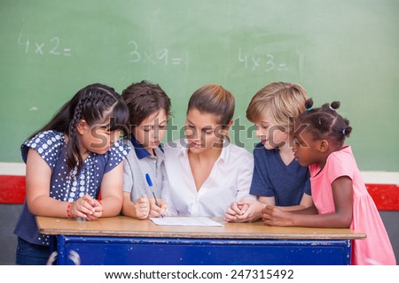 Attractive young female teacher checking multi race classroom work with other students at the desk.