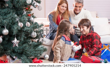 Brother and sister exchanging Christmas gifts in front of their parents. Happy family and holiday concept.