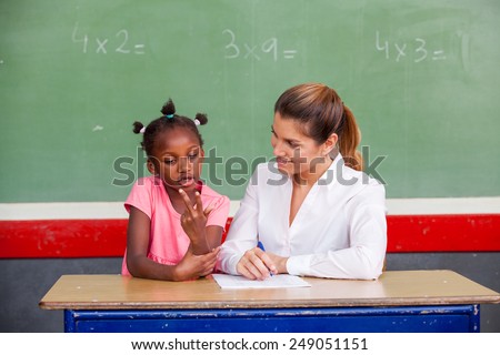 Happy female teacher and afro american schoolgirl discussing math questions in front of chalkboard.
