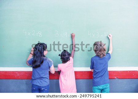 Multi ethnic schoolmates writing math at chalkboard.