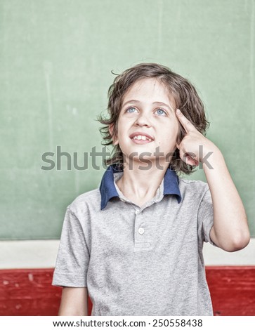 Happy primary school student thinking about the answer in front of chalkboard.