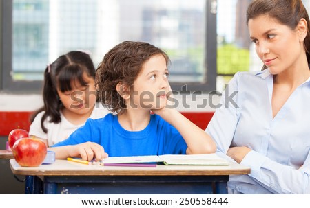 Teacher and schoolboy looking each other in primary classroom.