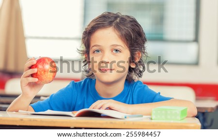 Happy elementary pupil touching his apple and reading book.