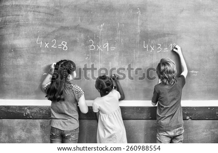 Interracial students writing numbers on chalkboard at elementary school.