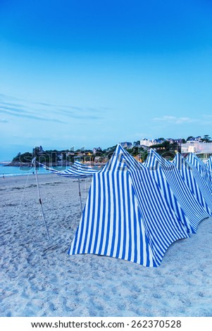 White and blue tents on the beach at sunset.