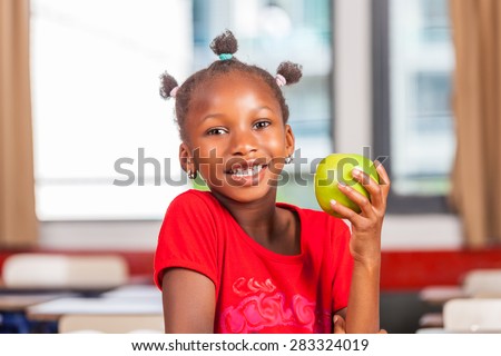 African girl at school holding green apple fruit.
