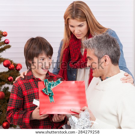 Child receiving Christmas gift from parents at home.